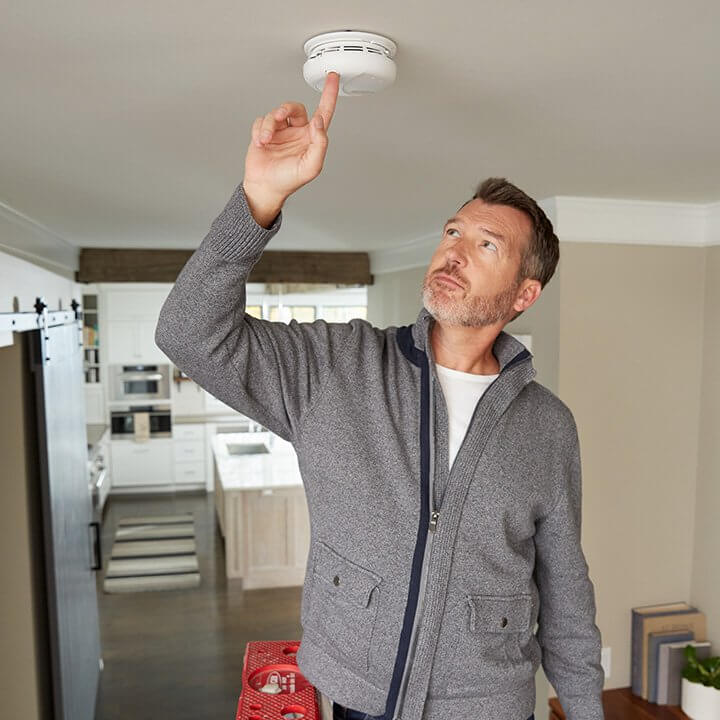A man tests a smoke alarm on his home ceiling.