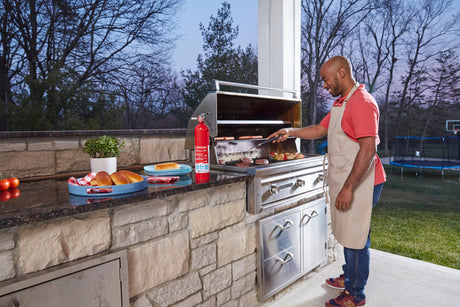 A man barbecues food on a gril, with a fire extinguisher close by.