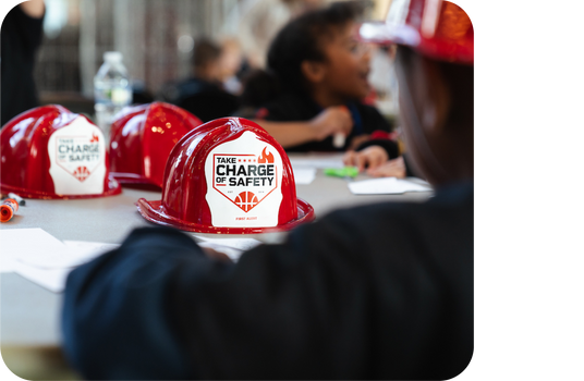 Children sit at a table where there are fire helmets with labels that read: Take Charge of Safety.